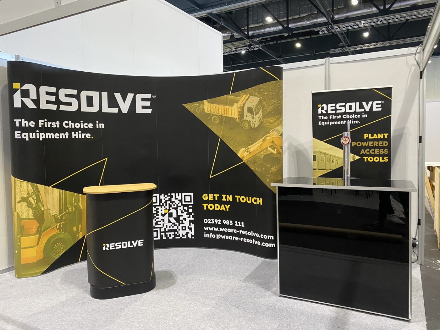 Trade show booth for "Resolve," featuring black and yellow displays with images of heavy equipment and contact information, including a QR code.